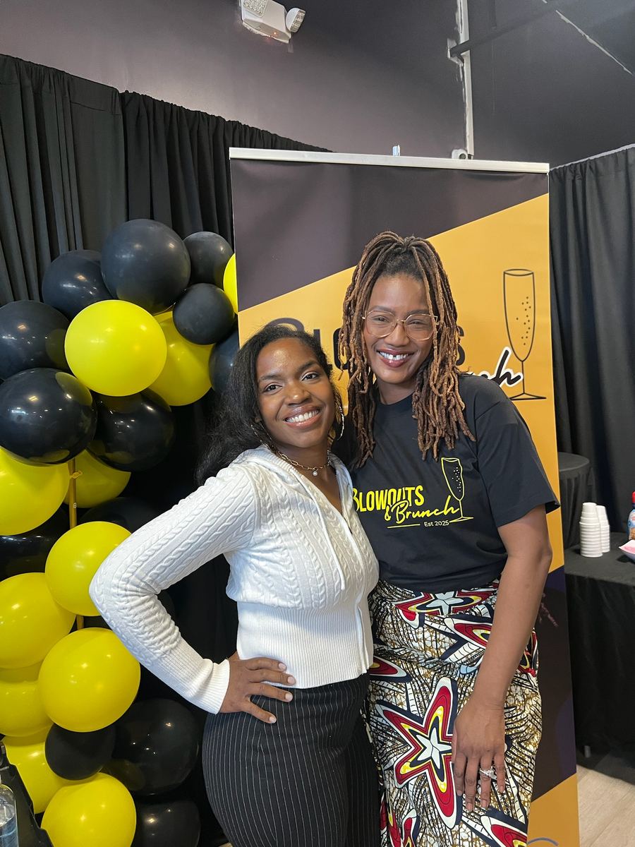Two guests smiling together in front of the Blowouts & Brunch banner