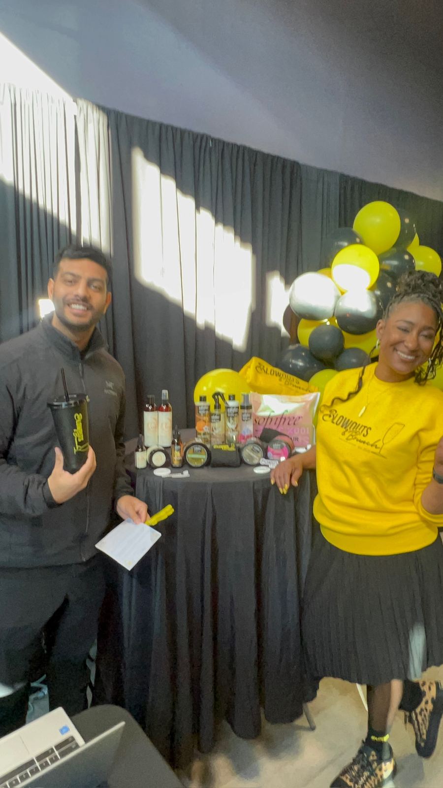 Attendees beside a table of hair care products and black and yellow balloons